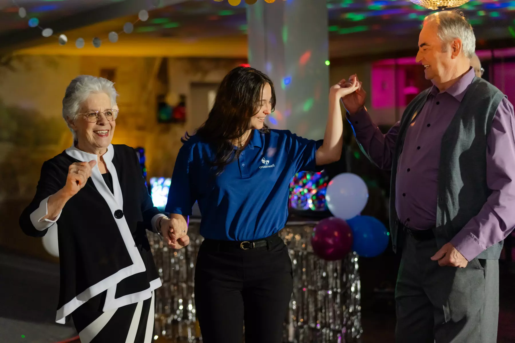 A senior couple and a Chartwell staff are enjoying a dancing party under disco light / Un couple de seniors et un membre du personnel de Chartwell profitent d'une soirée dansante sous la lumière du disco